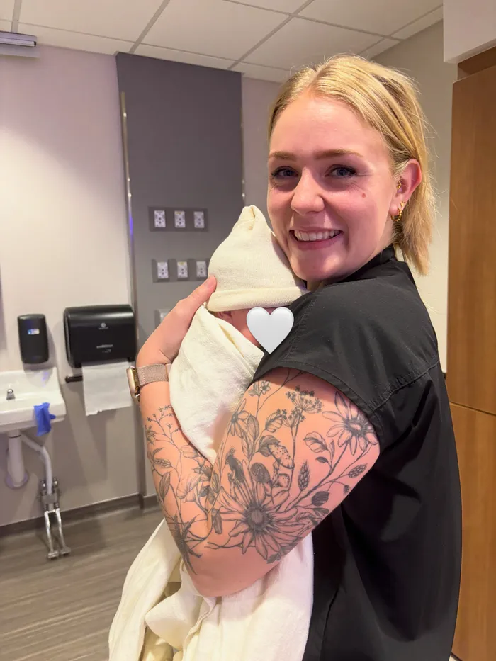 Jessica Bair smiling while holding a swaddled newborn