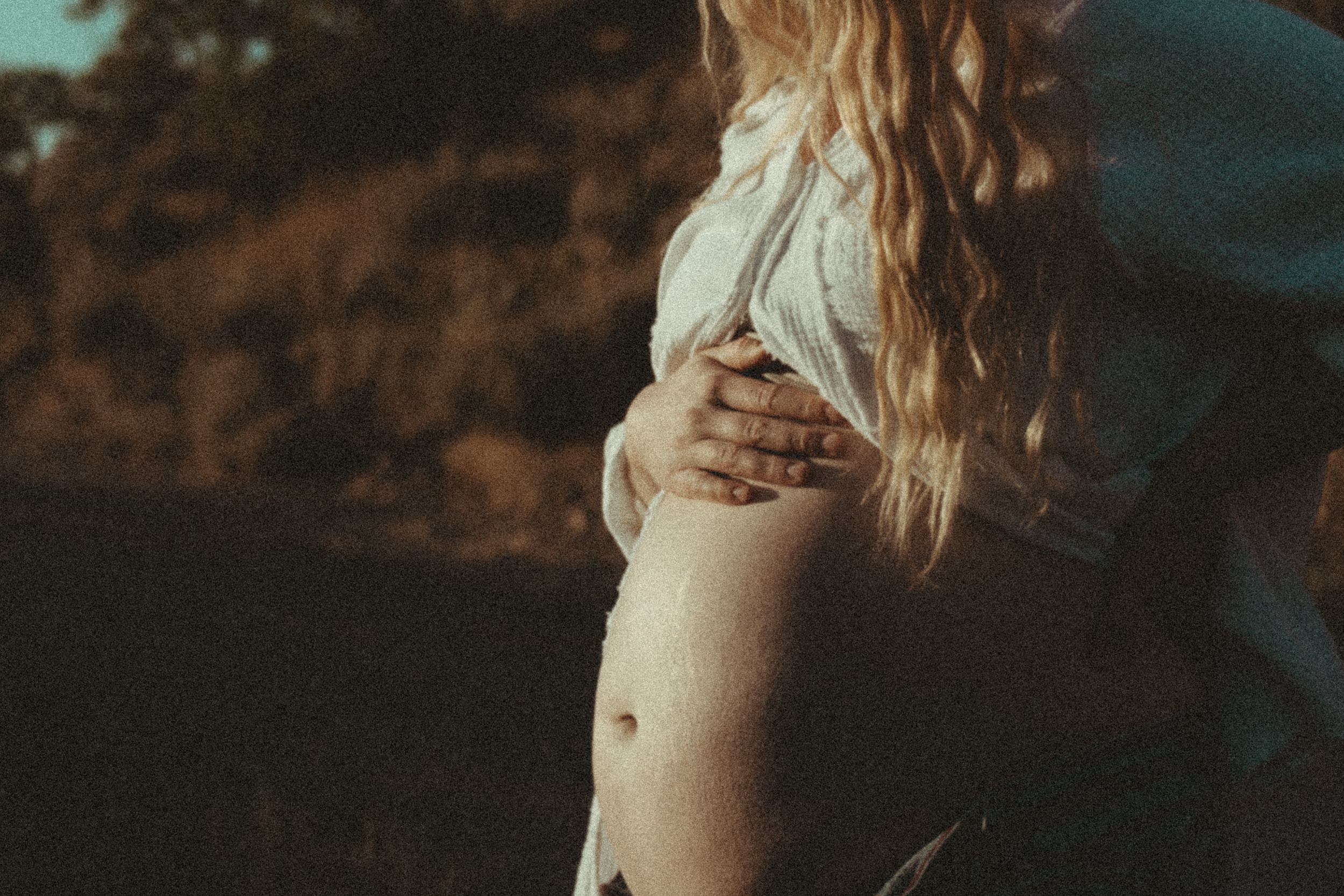 A pregnant client cradling her belly outdoors at golden hour